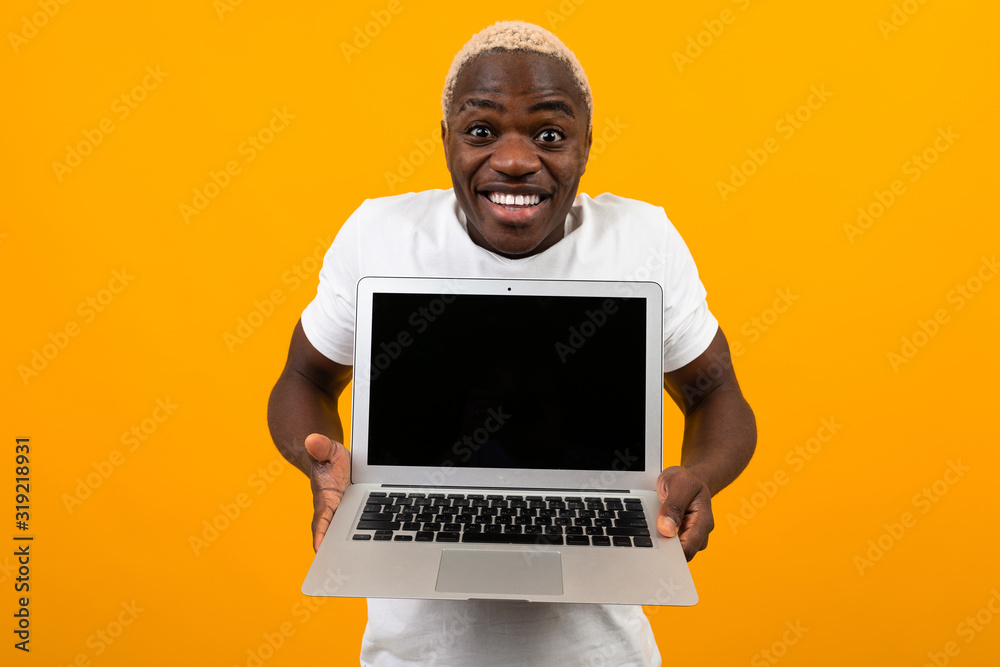 attractive joyful surprised american man in a white t-shirt with a beautiful smile stretches his arms with a laptop with a layout on a yellow background attractive joyful surprised american man in a white t-shirt with a beautiful smile stretches his arms with a laptop with a layout on a yellow background