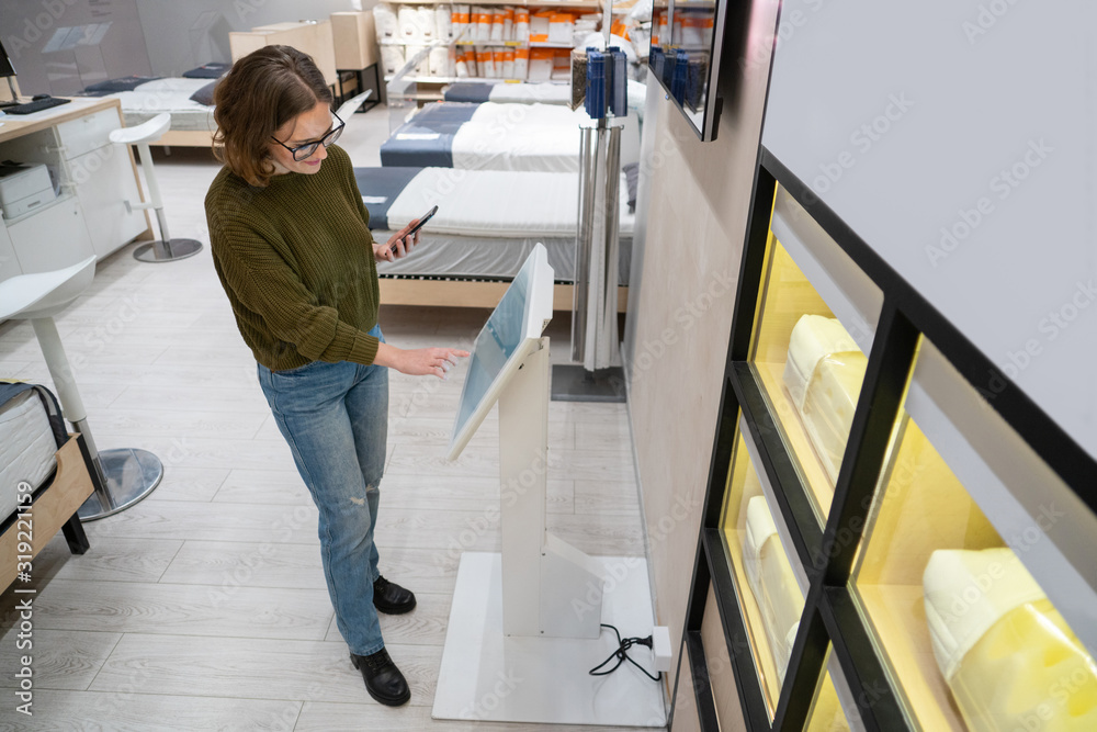 Woman with phone configuring furniture at the self-service desk in the store Woman with phone configuring furniture at the self-service desk in the store