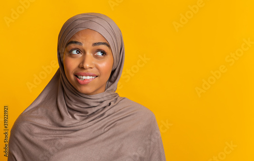 Doubtful black muslim woman in headscarf biting lip and looking aside © Prostock-studio