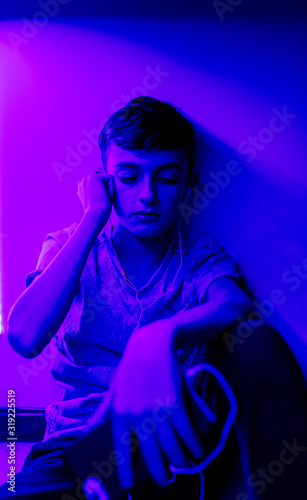 A young boy listening to music in his bedroom with LED lights on.