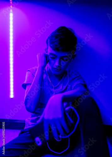 A young boy listening to music in his bedroom with LED lights on.