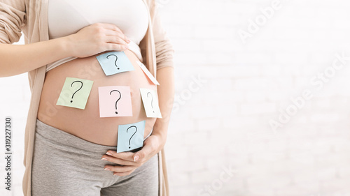Pregnant woman with question marks on paper stickers on tummy