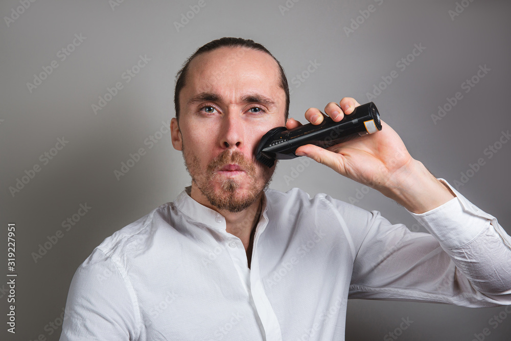 Man shaving face with electric razor on gray Man shaving face with electric razor on gray