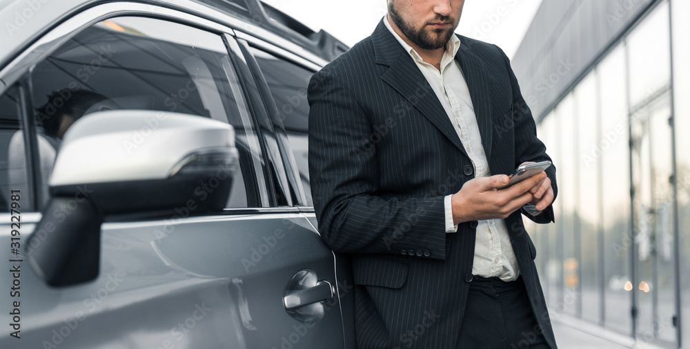 Handsome businessman with smartphone near vehicle on office parking Handsome businessman with smartphone near vehicle on office parking