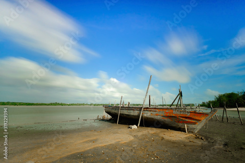 Fototapeta Naklejka Na Ścianę i Meble -  An old wooden fishing boat stranded on the beach on a sunny day with a beautiful sky