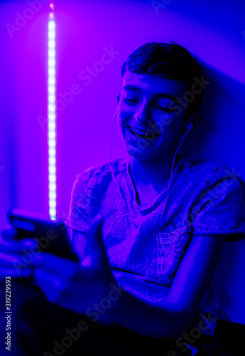 A young boy listening to music in his bedroom with LED lights on.