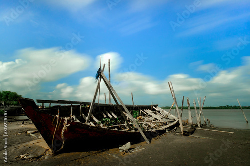 An old wooden fishing boat stranded on the beach on a sunny day with a beautiful sky