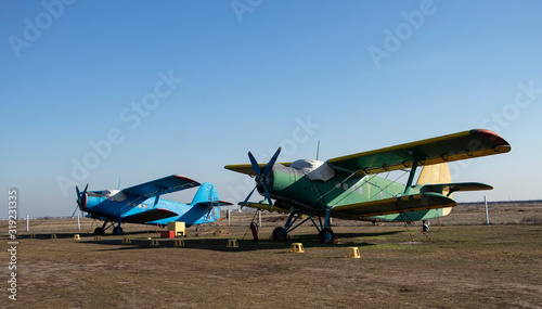 Old airplanes. Green and blue corncob. Sports plane of the 19th century. Until now they fly. Touch the antiquity. Propeller and wings. Airplane repair. Aerodrome. Blue sky. Sunny.