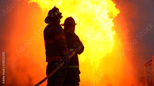 Silhouette of two firefighters burning a large tank of oil