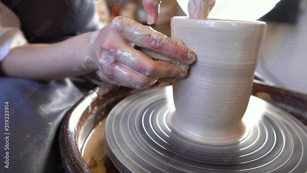 Potter working on a Potter's wheel making a vase. Woman forming the clay with her hands creating jug in a workshop. Potter working on a Potter's wheel making a vase. Woman forming the clay with her hands creating jug in a workshop.