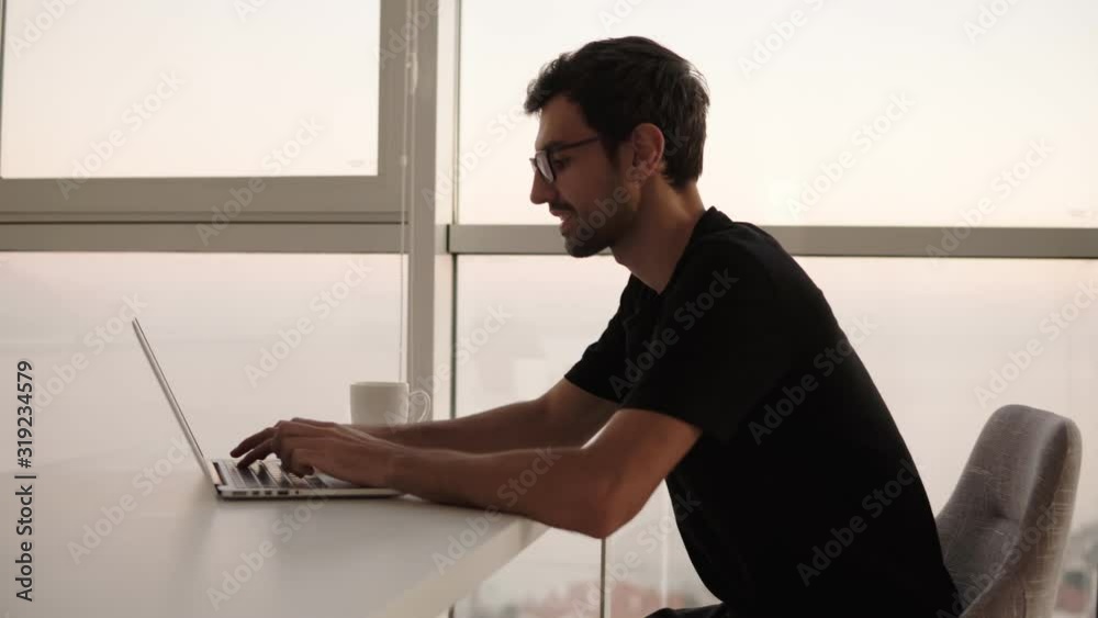 Side view of business man using laptop computer at remote workplace in slow motion. Freelancer working on computer at home. Focused man looking on screen and actively typing at big house with Side view of business man using laptop computer at remote workplace in slow motion. Freelancer working on computer at home. Focused man looking on screen and actively typing at big house with
