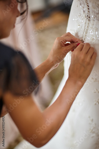 bridesmaids help the bride to wear a wedding dress
