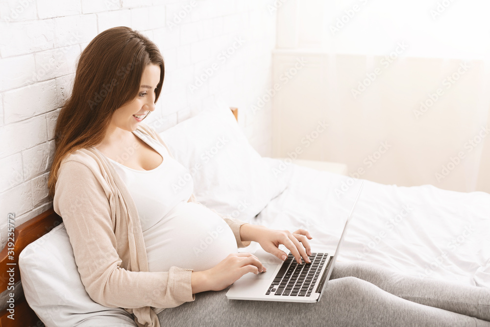 Happy pregnant blogger typing content on laptop Happy pregnant blogger typing content on laptop