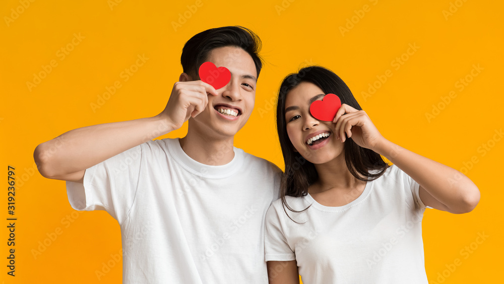 Happy asian couple covering one eye with valentine cards - obrazy, fototapety, plakaty 