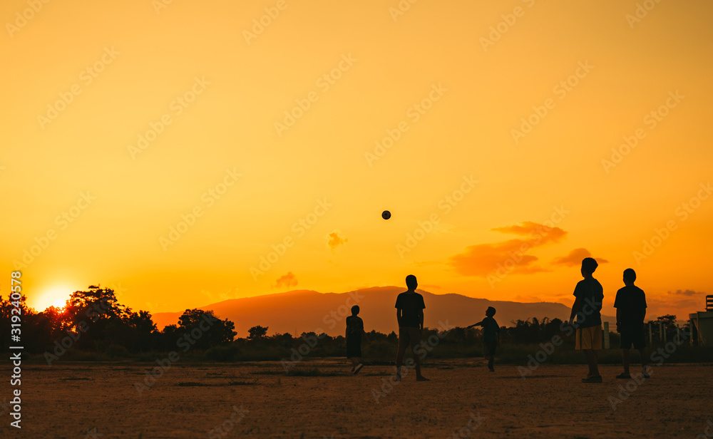 Fototapeta premium Silhouette action sport outdoors of kids having fun playing soccer football for exercise in community rural area under the twilight sunset. Picture with copy space.