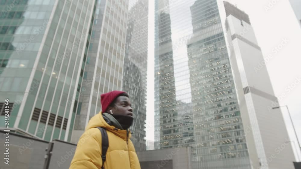 Low angle view of African young man wearing wireless headphones going in urban area Low angle view of African young man wearing wireless headphones going in urban area