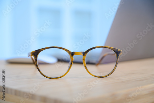Close up of eye glasses on work desk with mouse and laptop at business workplace.