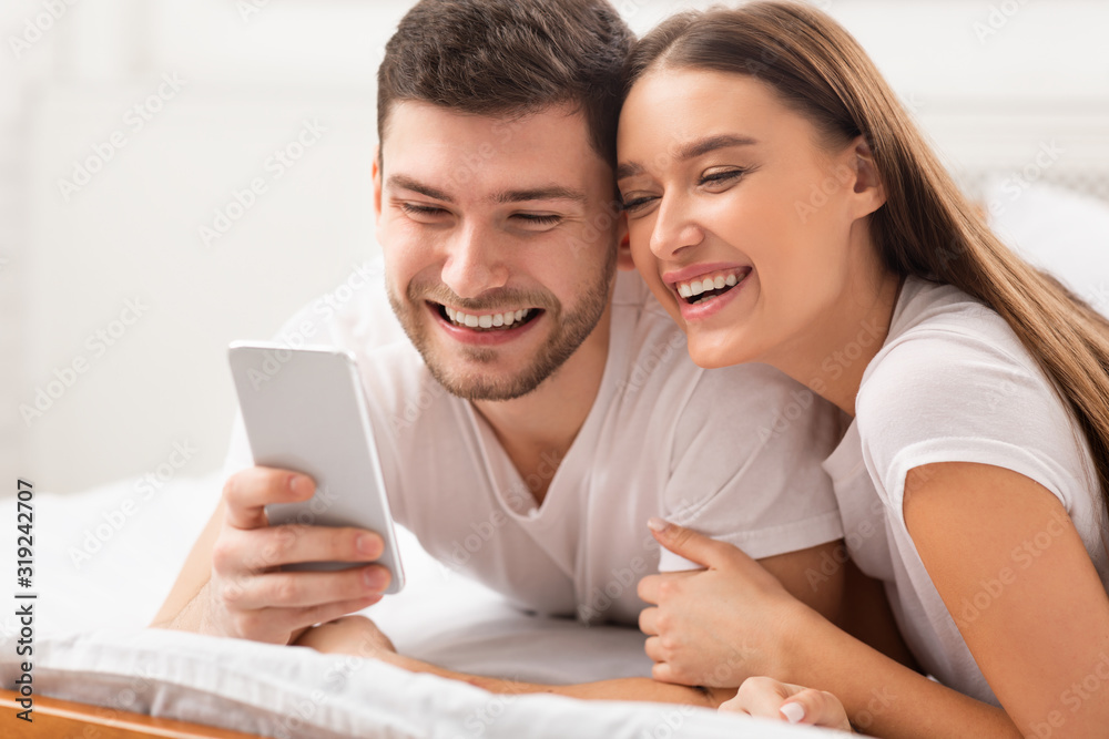 Cheerful Boyfriend And Girlfriend Using Phone Lying In Bed Indoor Cheerful Boyfriend And Girlfriend Using Phone Lying In Bed Indoor