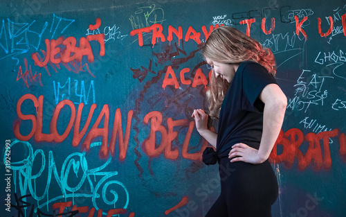 Photography Blonde girl leaning against a graffiti wall