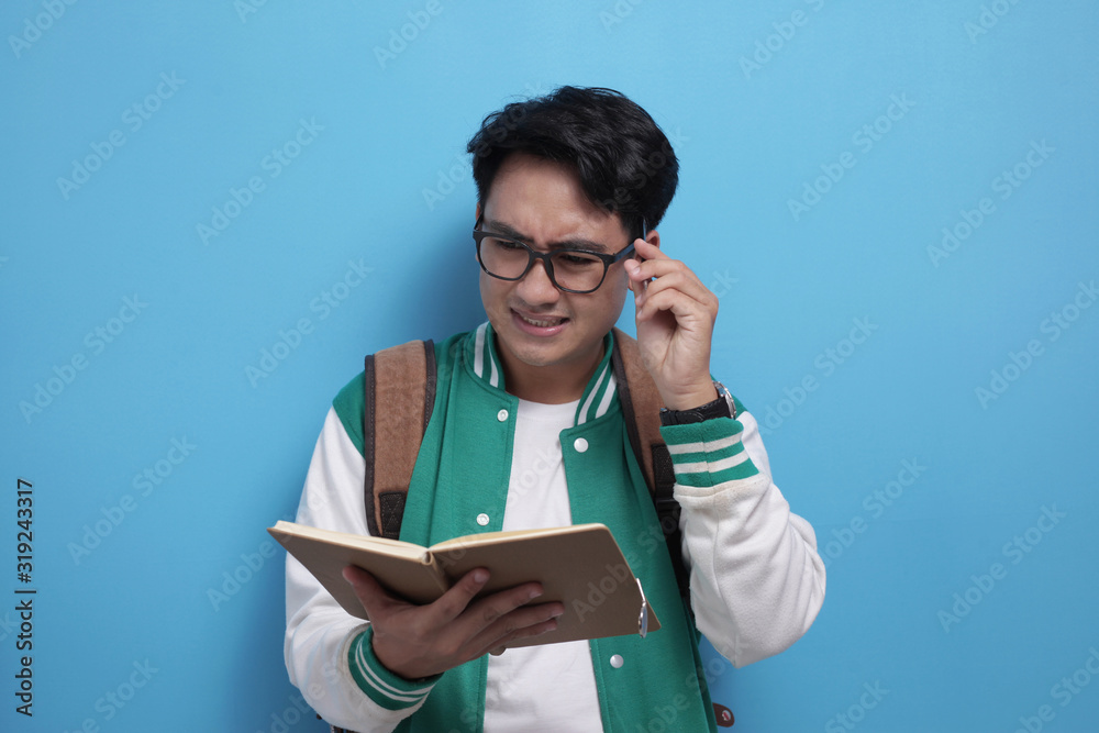 Male Asian student studying hard, reading a book against blue background Male Asian student studying hard, reading a book against blue background