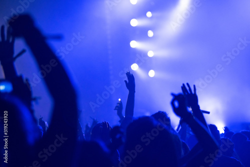 Silhouette of raised arms, crowd of people in the front of bright stage lights at concert