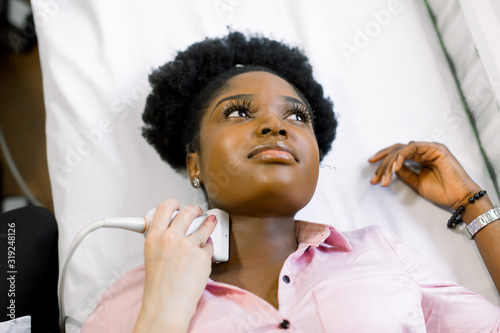 Close-up portrait of young African woman patient during the ultrasound examination of a thyroid lying on the couch in medical office