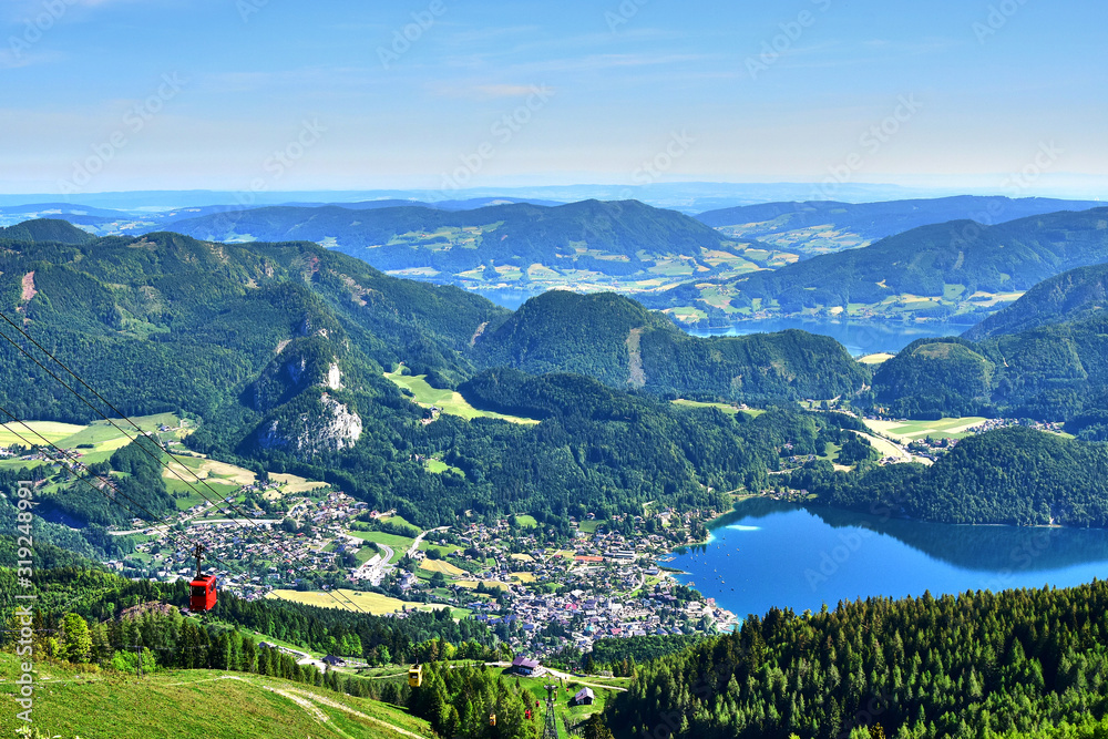 Zwolferhorn, green mountains and fields in Austria, trees and lakes, a bird's-eye view of the city, in the spring afternoon.
