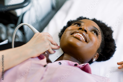 Close up shot of a young smiling African American woman getting her neck and thyroid gland examined by doctor using ultrasound scanner at the modern clinic