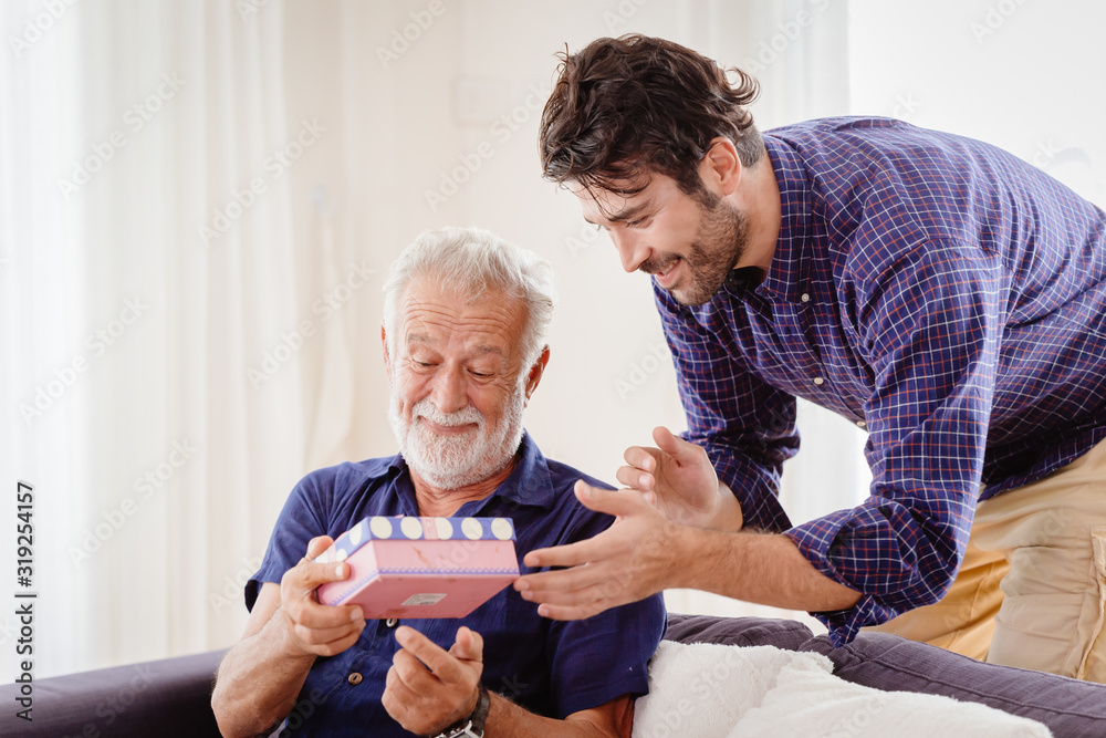 elder happy greeting with gift box present from his son sitting in living room.