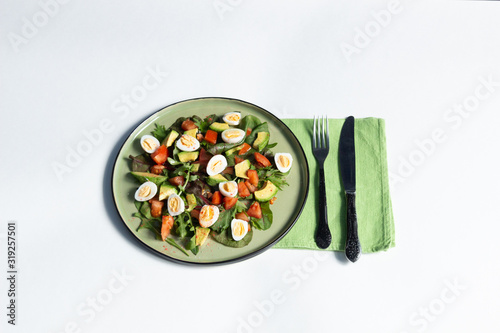 fresh salad with green leaves, eggs, tomato, avocado in a plaate with fork and knife on white background photo