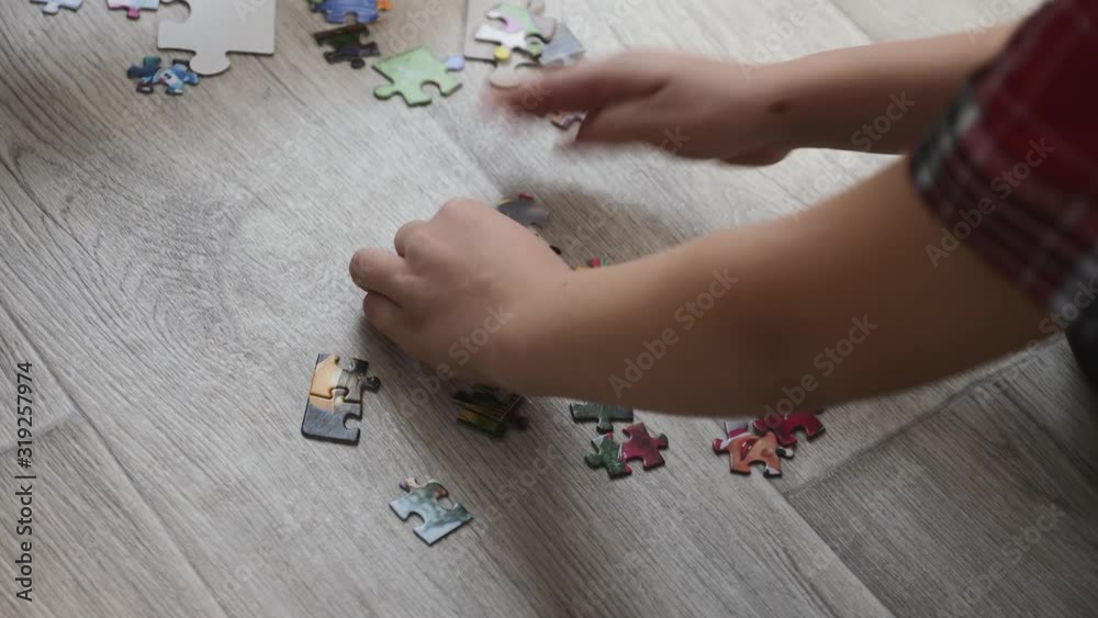 A young mother with a blond son is sitting on the floor of the room. A happy family puts together a puzzle. Mom helps the child. A young mother with a blond son is sitting on the floor of the room. A happy family puts together a puzzle. Mom helps the child.