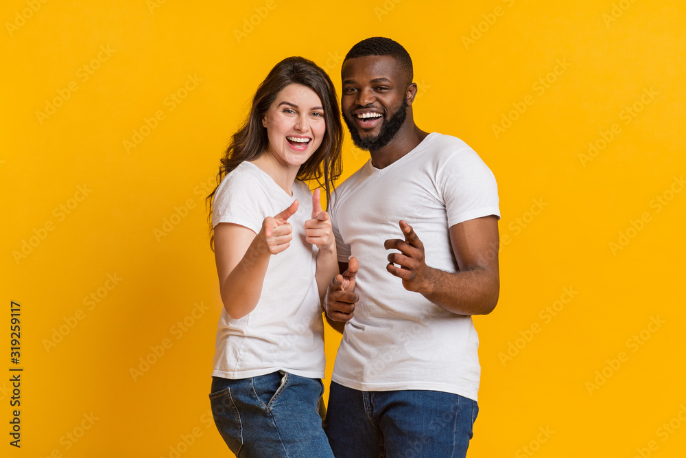 Joyful interracial lovers indiciting fingers at camera and laughing Joyful interracial lovers indiciting fingers at camera and laughing