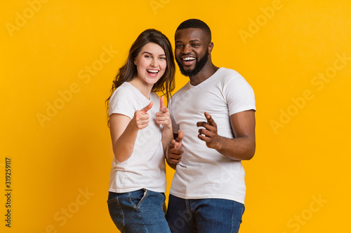 Joyful interracial lovers indiciting fingers at camera and laughing