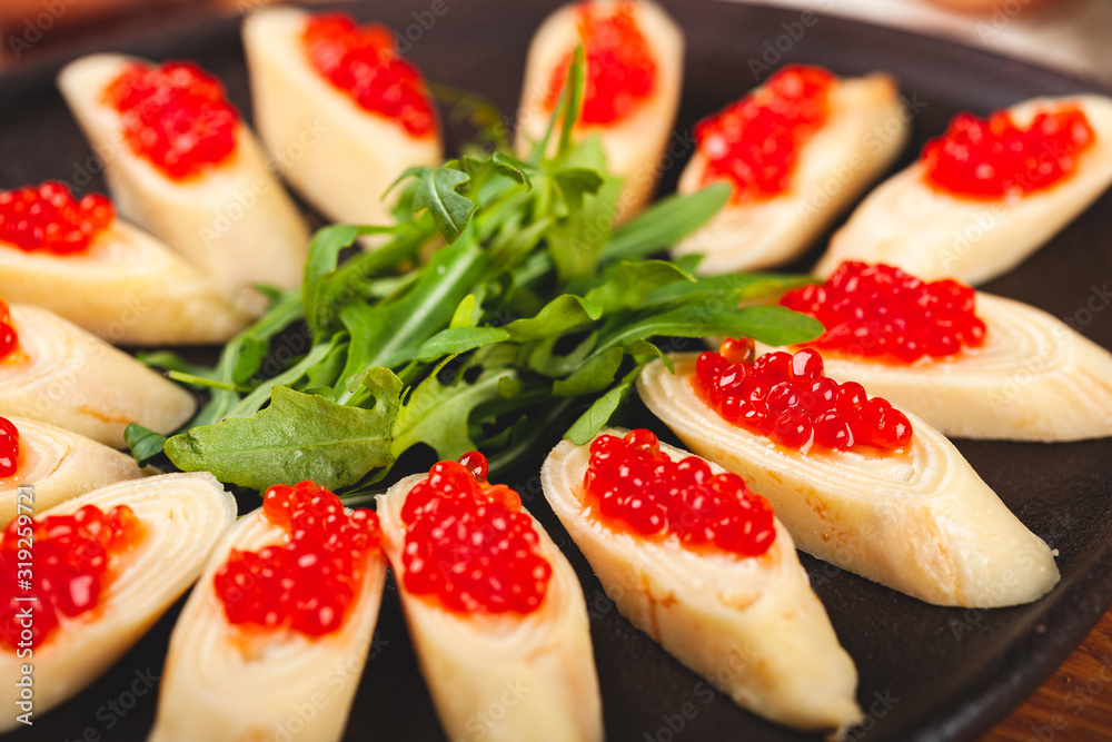 Rolled crepes (pancakes, blini) with red caviar served with arugula on black plate. Rolled crepes (pancakes, blini) with red caviar served with arugula on black plate.
