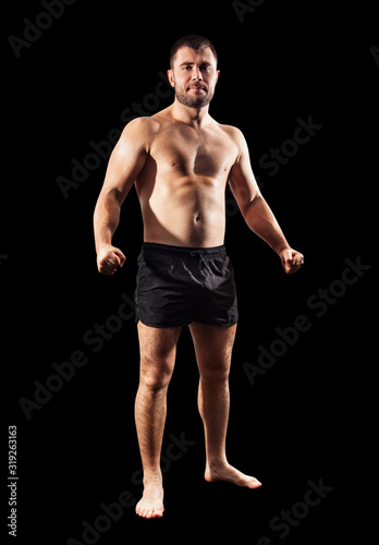Brutal muscular sportsman standing in black shorts.