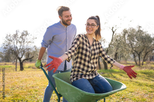 Giovane coppia sorridente si diverte mentre fa giardinaggio con una cariola photo