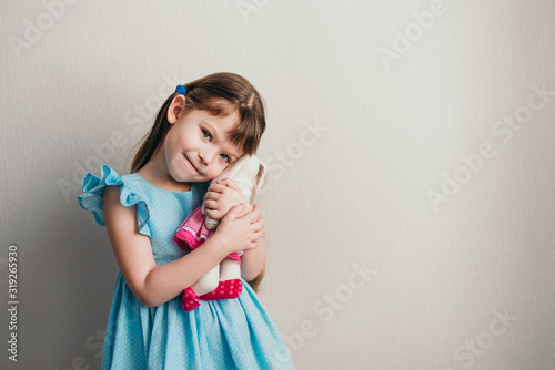 Pretty little girl in blue dress looks at camera and holds her toy rabbit copyspace