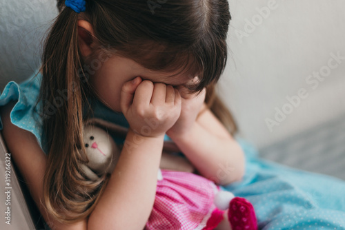 Sad little girl crying covering her face with hands closeup