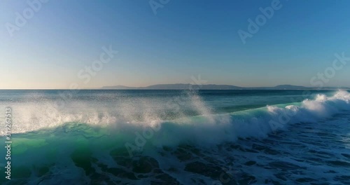 Aerial view of waves breaking at the Comporta Beach with the Arrabida mountains on the background, in Portugal