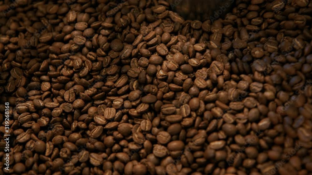 Close up slow motion cinematic beautiful shot of brown roaster coffee beans spinning and mixing in drum roaster on slow speed. Roasting proccess of small batch brewery