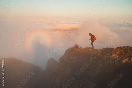 Hiker watching a Brocken spectre up in the mountains after sunrise