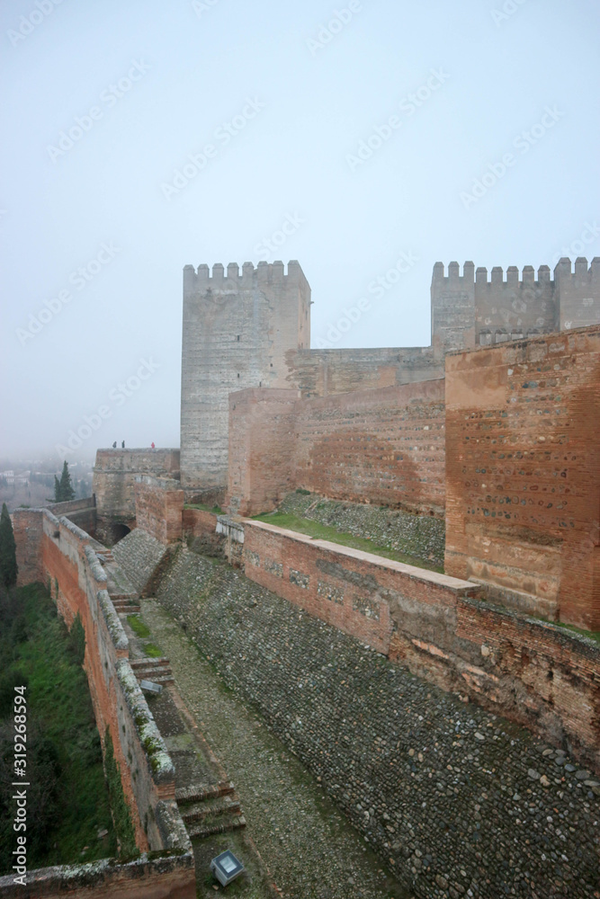 Walls and towers of medieval citadel fortress of Alhambra, Granada, Spain in the morning fog