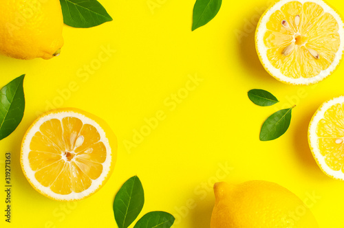 Creative background with fresh lemons and green leaves on bright yellow background. Top view flat lay copy space. Lemon fruit citrus minimal concept vitamin C. Composition with whole, slices of lemons