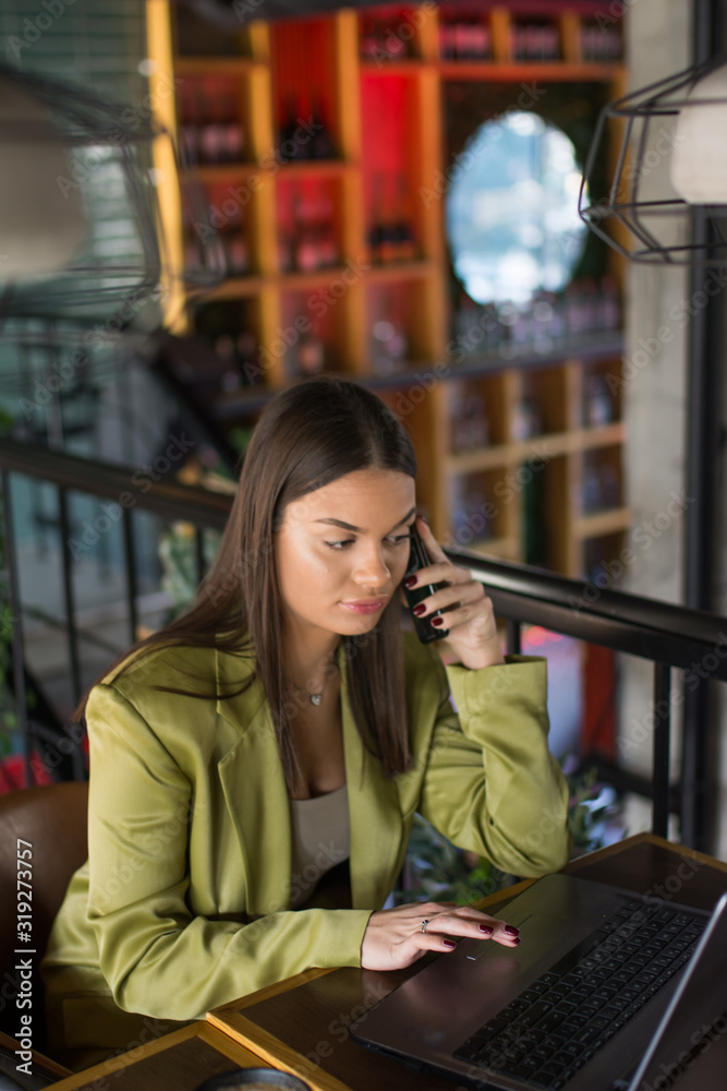 Fototapeta premium Young businesswoman using laptop and cell phone at table in a cafe