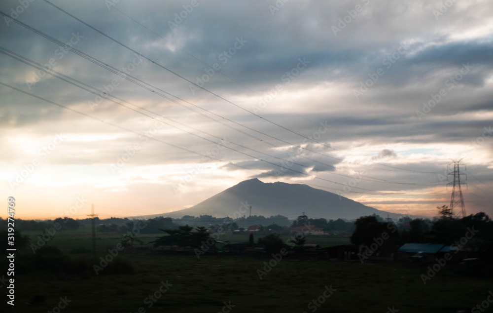 Sunrise and morning mist on the countryside outside of Manila in the Philippines, with the volcano far away in the distance and with the power lines as silhouettes
