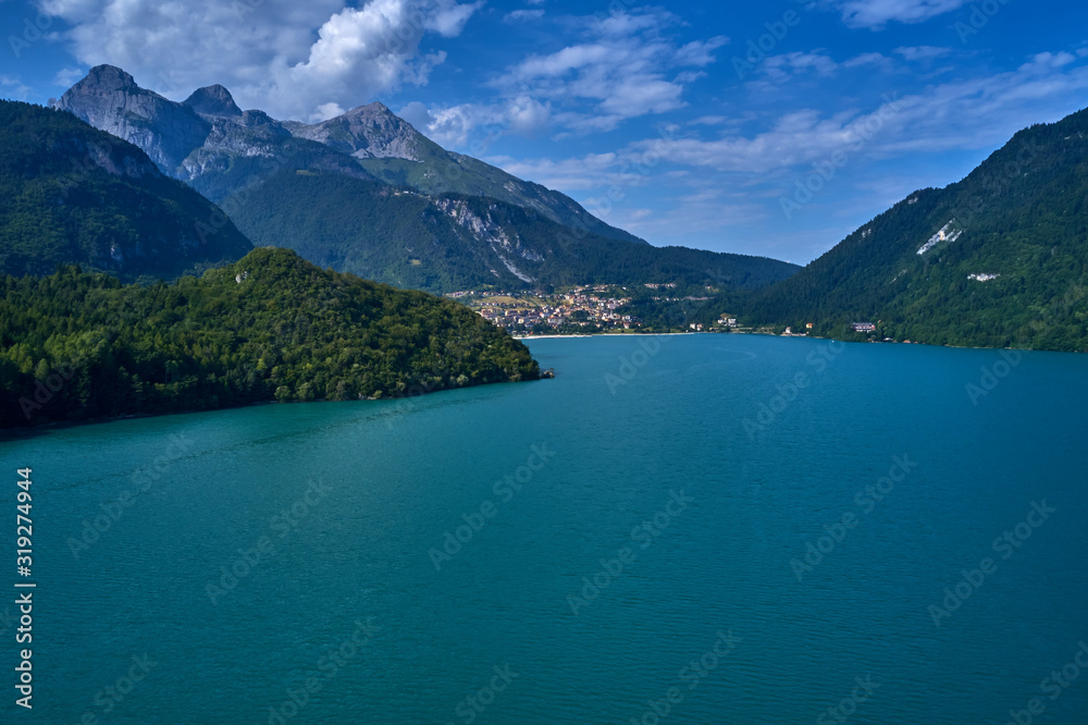 Aerial view of Lake Molveno, north of Italy in the background the city of Molveno, Alps, blue sky. Reflection of mountains in water. 