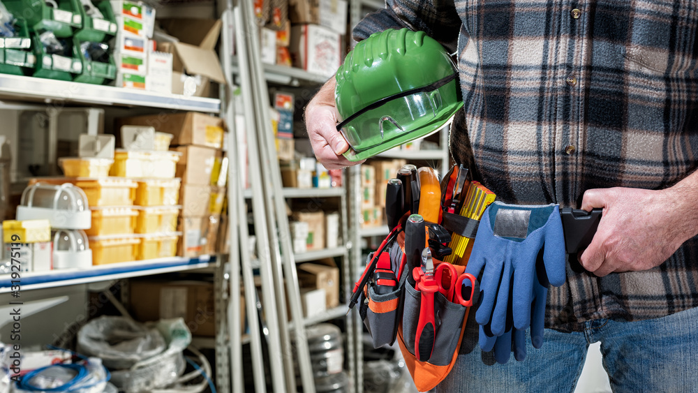 Electrician in the electrical component store holds the helmet and goggles in his hand. Construction industry, electrical system. Electrician in the electrical component store holds the helmet and goggles in his hand. Construction industry, electrical system.