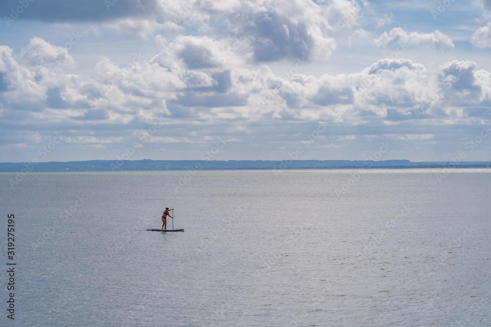 Luc-Sur-Mer, France - 08 16 2019:  View of the sea from the beach with a paddling woman