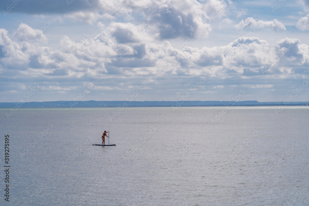 Fototapeta premium Luc-Sur-Mer, France - 08 16 2019: View of the sea from the beach with a paddling woman
