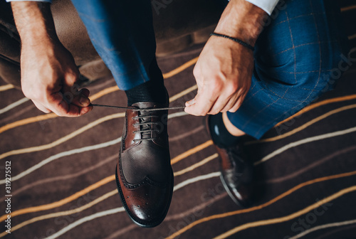 Close-up of a man, groom, businessman tying shoelaces on brown expensive shoes. Morning businessman preparing for work. Photography, concept.